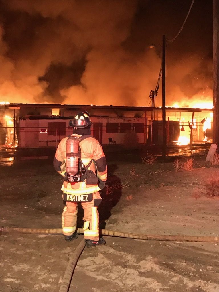Firefighter Martinez in full turnout gear and SCBA facing a fully involved structure fire